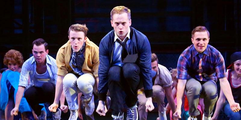 Seven student actors/actresses crouching knees together, arms straight/at sides in triangle formation during a performance